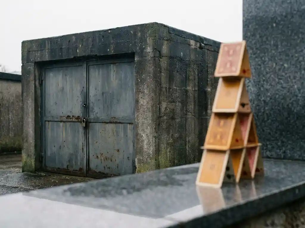 beton-garage-kartenhaus-stabilitaet-vergleich.jpg Massiver Betongarage mit schweren Stahlttüren neben einem instabilen Kartenhaus auf Steinoberfläche, Vergleich von Stabilität und Fragilität.